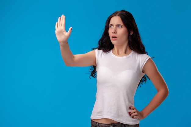 Studioportret van een jonge mooie vrouw in een wit t-shirt tegen een blauwe muurachtergrond. Mensen oprechte emoties.