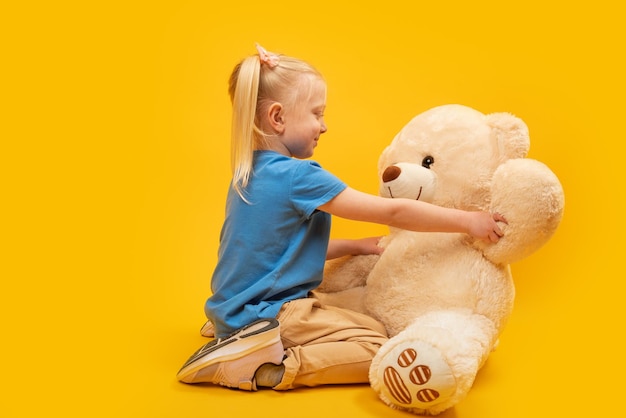 Studioportret van een klein meisje met een grote teddybeer op gele achtergrond kind speelt met zacht stuk speelgoed