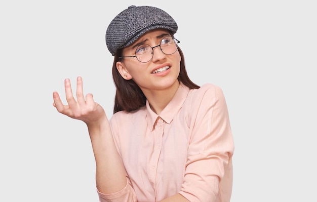 Studioportret van een ondervraagde jonge vrouw die serieus kijkt naar het bespreken van dingen gekleed in een casual trendy outfit die zich voordeed op een witte muur Student meisje heeft een verwarde uitdrukking Mensen emoties