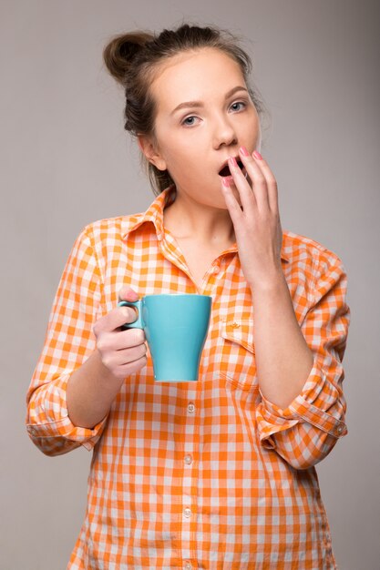 Studioportret van een slaperige vrouw in een oranje overhemd met een in hand kop van koffie