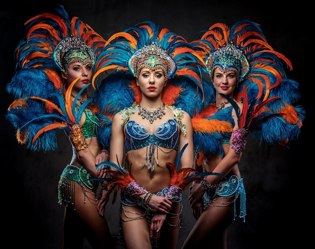 Studioportret van een vrouwelijke groep professionele dansers in kleurrijke weelderige kostuums van carnavalveren. geïsoleerd op een donkere achtergrond.