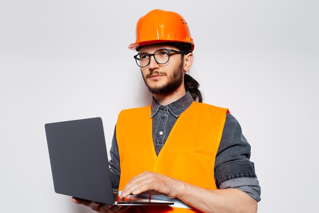 Studioportret van ingenieur die laptop vasthoudt in oranje bouwmachines