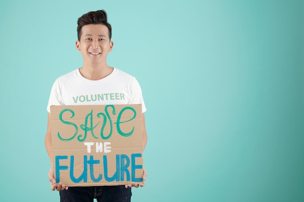 Studioportret van jonge glimlachende vrijwilliger met kartonnen bordje die mensen vraagt om de toekomst te redden