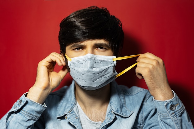 Studioportret van jonge zieke kerel in spijkerjasje, medisch gezichtsmasker tegen coronavirus