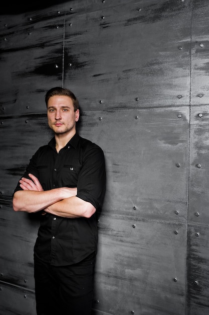 Foto studioportret van stijlvolle man draagt zwart shirt tegen stalen muur