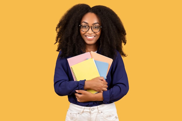 Photo studious young black woman with glasses and colorful notebooks