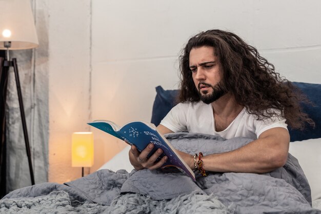 Foto studio delle stelle. giovane serio seduto sul letto mentre legge un libro di astrologia