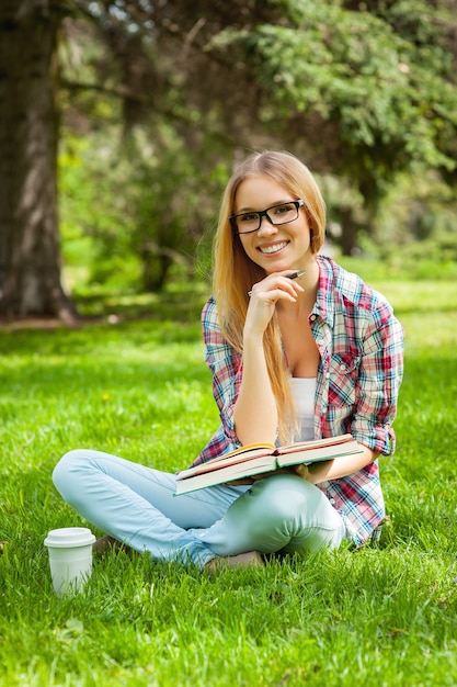 Studiare all'aria aperta. bella giovane studentessa che tiene la mano sul mento e sorride mentre è seduta in un parco