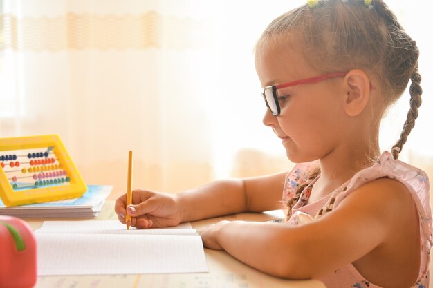 Studiare a casa, ritratto di una ragazzina seduta a una scrivania con gli occhiali.