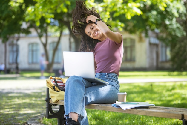 Foto studiare al parco. una ragazza con una maglietta rosa con un laptop nel parco