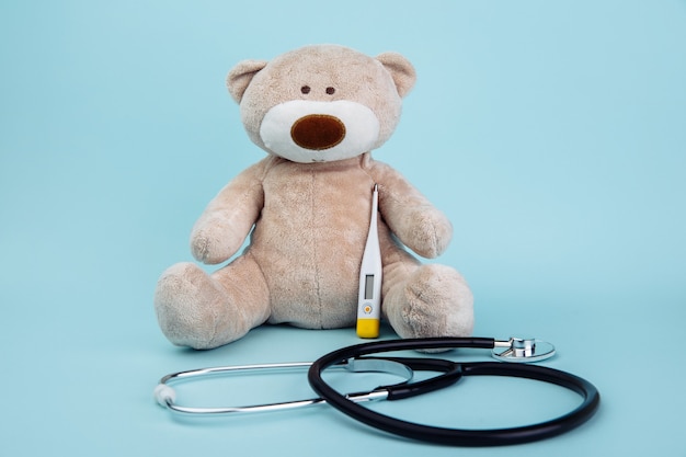 Stuffed Bear animal presented as a pediatrician holding a thermometer isolated on blue.