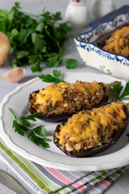 Melanzane ripiene al forno con formaggio e aglio su piatto bianco su sfondo grigio chiaro