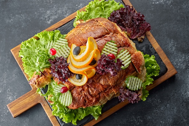 Stuffed fish on a wooden board, with herbs and vegetables, against a dark background