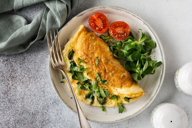 Stuffed omelette with tomatoes, red bell pepper, cream cheese and corn or lamb's lettuce on light concrete with copy space. Healthy diet food for breakfast. Top view, flat lay.