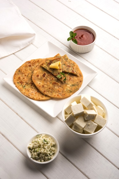 Photo stuffed paneer paratha with melting butter, served with fresh cottage cheese cubes and tomato ketchup. selective focus