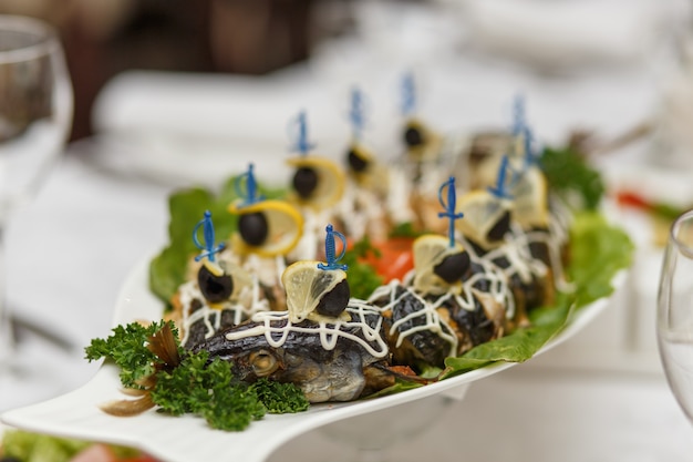 A stuffed pike with vegetables on the table. Each slice is strung on a skewer with olive and lemon.