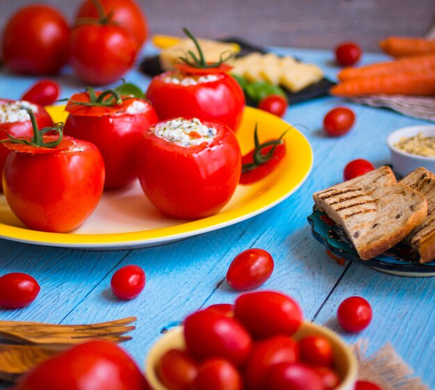 Stuffed tomatoes with cheese, and different vegetables on a wooden table