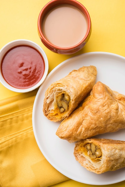 Stuffed vegetable puff or samosa, famous Indian Bakery snack, served with Tomato Ketchup and hot tea, selective focus