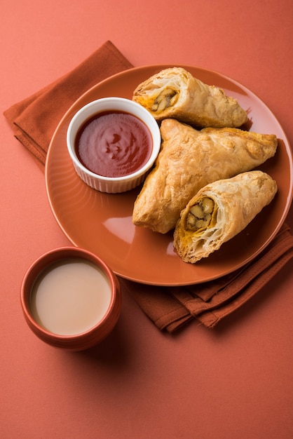 Stuffed vegetable puff or samosa, famous Indian Bakery snack, served with Tomato Ketchup and hot tea, selective focus