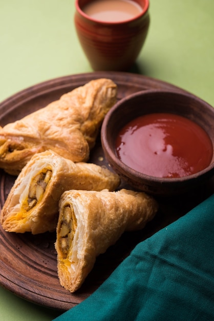 Stuffed vegetable puff or samosa, famous Indian Bakery snack, served with Tomato Ketchup and hot tea, selective focus