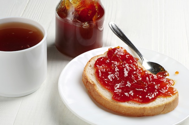 Stuk brood met jam en kopje thee op witte tafel