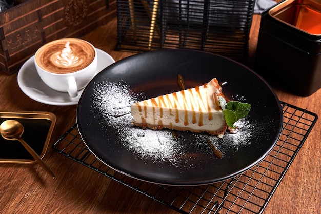 Foto stuk cheesecake op zwarte plaat op een tafel met munt en een kopje koffie zijaanzicht