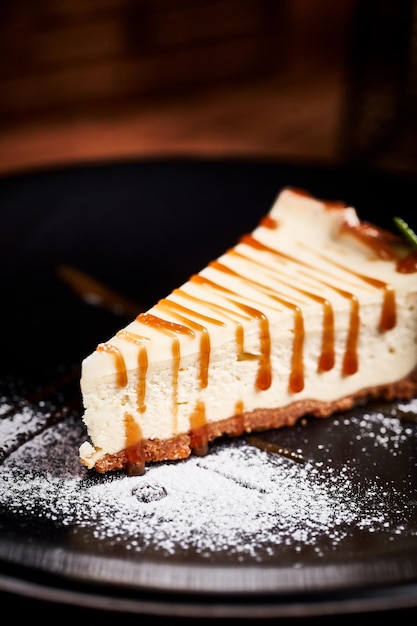 Foto stuk cheesecake op zwarte plaat op een tafel met munt en een kopje koffie zijaanzicht