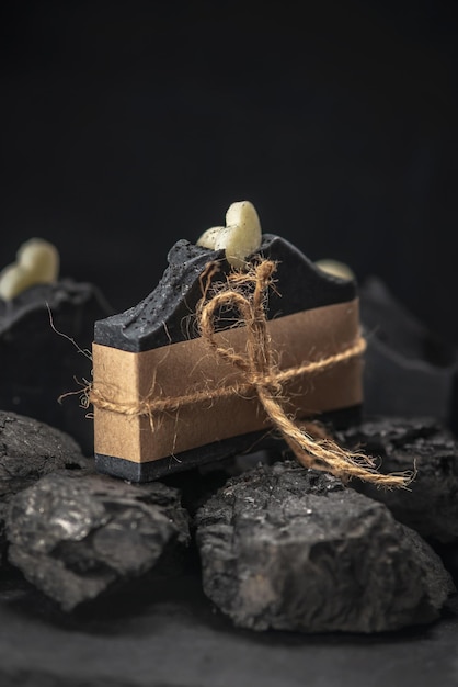 Stuk natuurlijke houtskoolzeep omwikkeld met ambachtelijk papier en touw op kolen op een zwarte achtergrond Concept van het maken en gebruiken van biologische zeep en cosmetica eco handgemaakte cadeaus