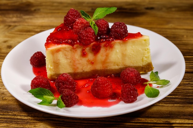 Stuk smakelijke New York cheesecake met frambozen en frambozenjam in een witte plaat op houten tafel