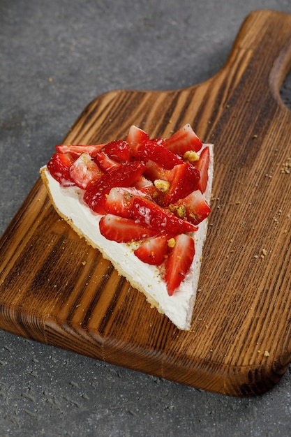 Foto stuk van cheesecake met aardbeien bovenop op houten houten plank