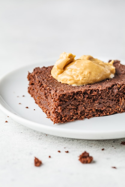 Stuk van de brownie van de veganistchocolade met pindakaas op witte plaat.