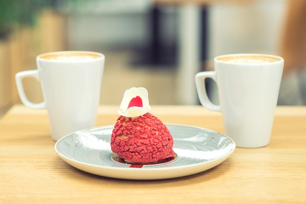 Stuk van rode taart met twee kopjes koffie op houten tafel in het café.
