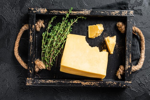 Stuk Zwitserse harde kaas in houten bakje. Zwarte achtergrond. Bovenaanzicht.