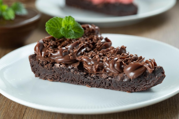 Stukje Chocolade Brownie Slice met Aardbeien en Chocolade Icing Houten tafel met munt en chocoladeschilfers op de achtergrond