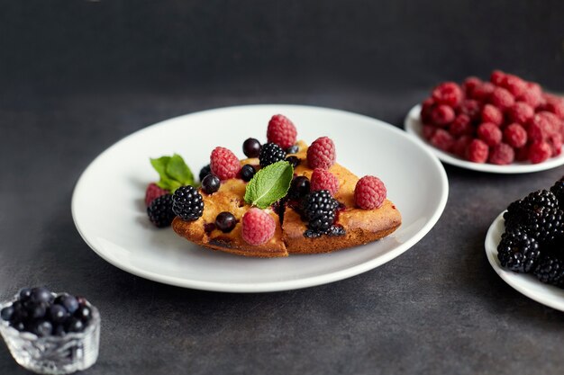 Stukje taart met bosbessen, frambozen en munt als dessert op een witte plaat, servet. Stukjes heerlijke zelfgemaakte cake op een tafel