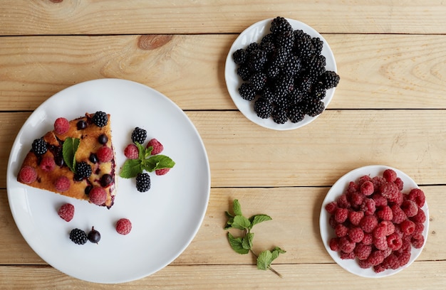 Stukje taart met bosbessen, frambozen en munt als dessert op een witte plaat, servet. Stukken van heerlijke zelfgemaakte cake op de tafel van een houten planken