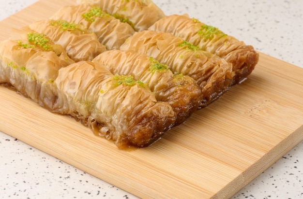 Stukjes gebakken baklava in honing en bestrooid met pistachenoten op een houten bord