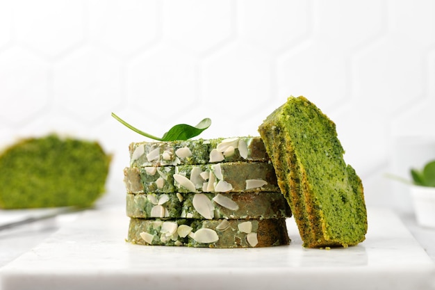 Stukjes groene sponscake met spinazie Groene taart met geschaafde amandelen gesneden op marmeren bord