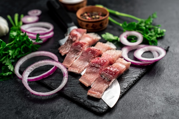 stukjes ingelegde haring op een mes met uien en kruiden op een stenen tafel