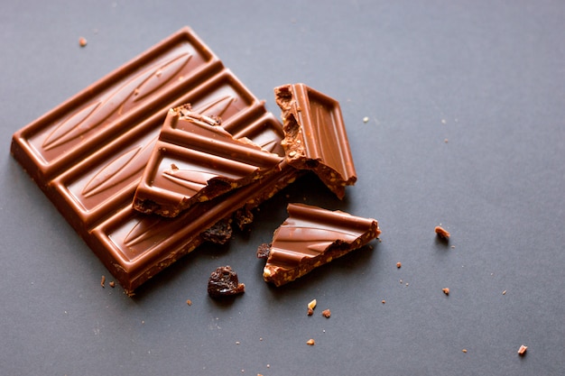 Foto stukjes melkchocolade met gemalen hazelnoten en rozijnen met alcohol op zwarte achtergrond