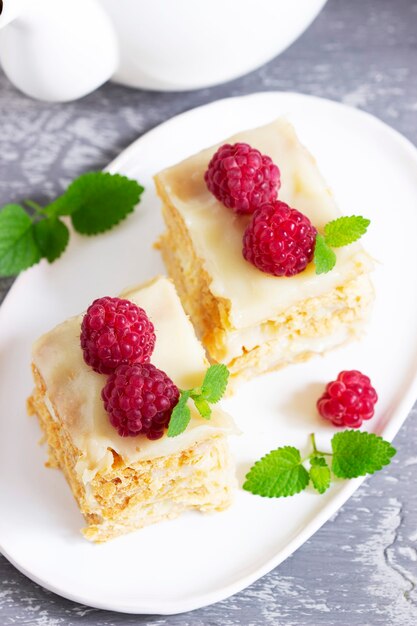 Stukjes Napoleon cake versierd met frambozen en citroenmelisse bladeren op een lichte achtergrond. Selectieve aandacht.