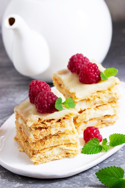 Stukjes Napoleon cake versierd met frambozen en citroenmelisse bladeren op een lichte achtergrond.