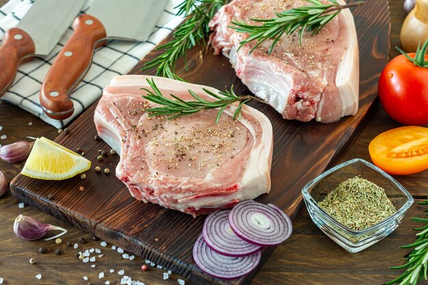 Stukjes rauw varkensvlees steak met specerijen en kruiden rozemarijn, zout en peper op houten achtergrond in rustieke stijl.
