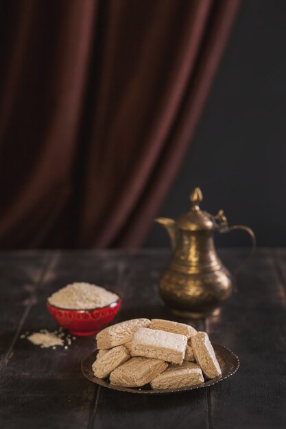 Stukjes tahini halva, sesamzaadjes in een kom, een vintage kan