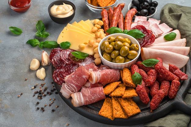 Stukjes vlees en worstjes van verschillende soorten, kaas en meer op een bord op een grijze achtergrond.