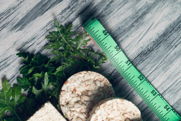 Stukken knäckebrood dichtbij meetlint en groene rucola op grijs.