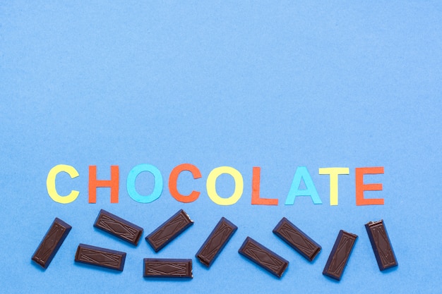 Stukken van chocolade en de inscriptie chocolade op een blauwe achtergrond