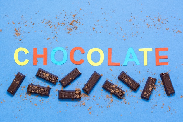 Stukken van chocolade en de inscriptie chocolade op een blauwe achtergrond
