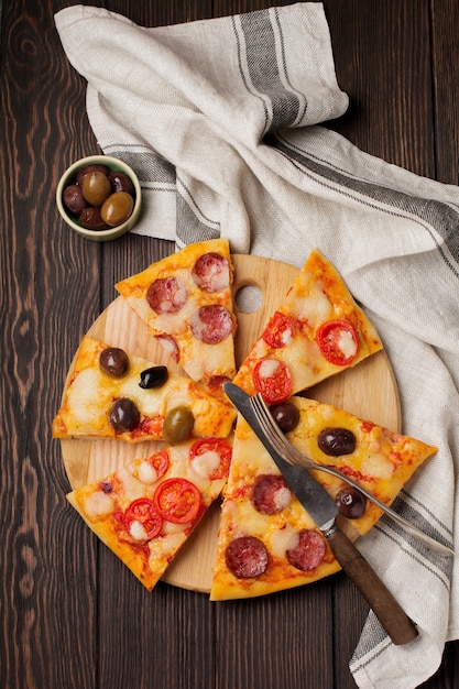 Stukken van verschillende griekse pizza's met olijven, italiaanse margarita en pepperoni op een donker houten rustiek.