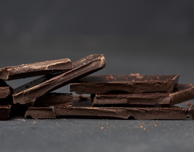 Stukken van zwarte chocolade op een zwarte achtergrond, zoete dessert